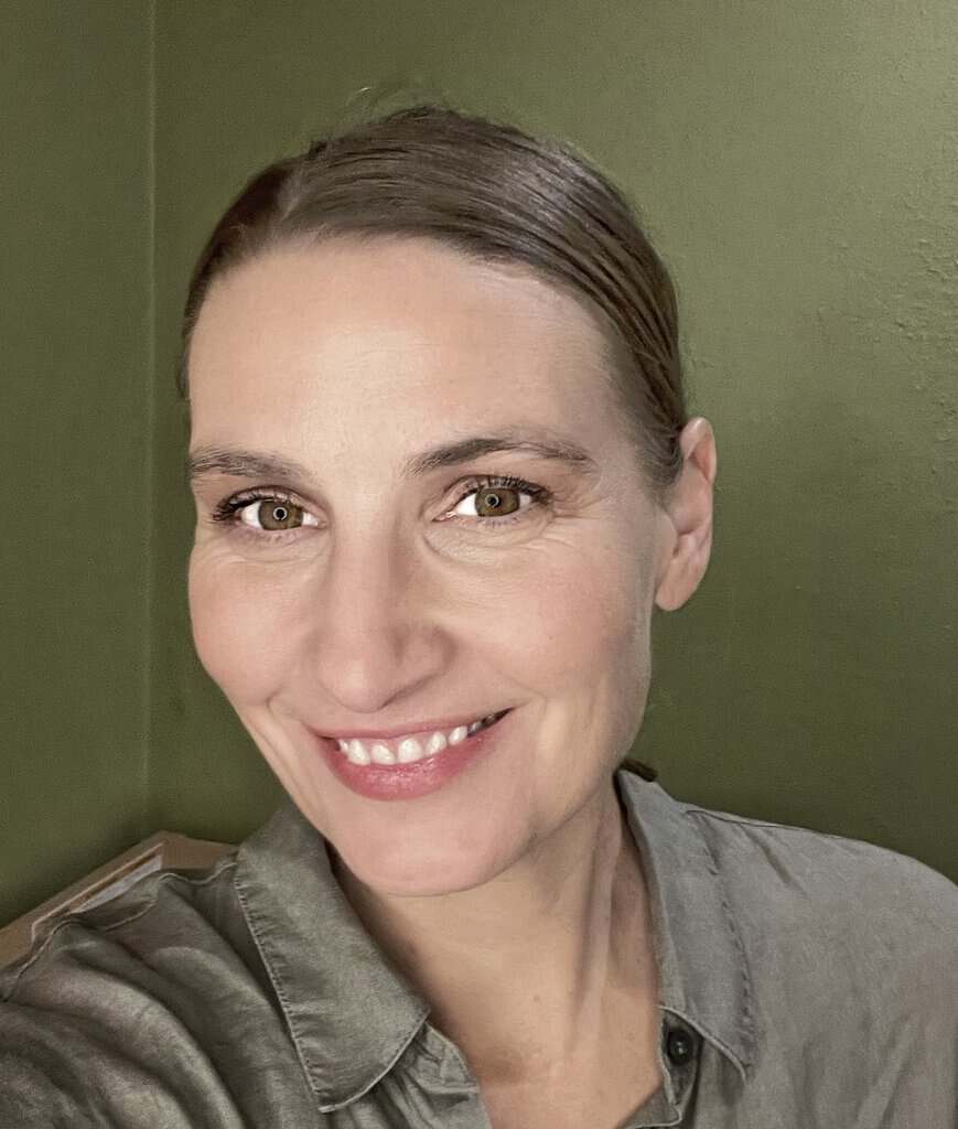 Anja Taylor smiling in front of an olive green wall.